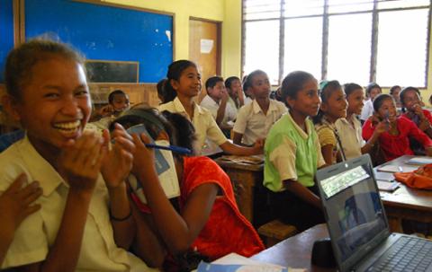 The students in the class are laughing and looking at the front of the classroom.