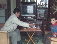 An old man and boy are sitting opposite to each other in front of the TV.