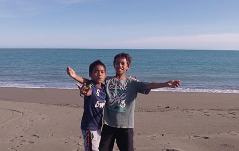 Two children stand on the beach with the sea behind them.